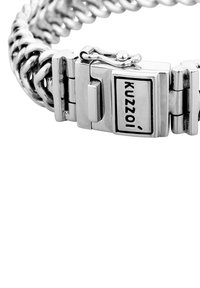 Sidabrinė grandinėlės apyrankė su sujungtais metaliniais žiedais, dėžutės tipo užsegimu su logotipu ir poliruotu paviršiumi. Kompaktiškas ir tvirtas dizainas.