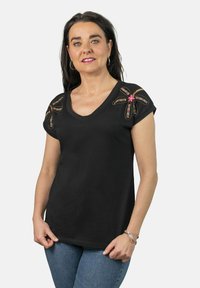 Camiseta negra de cuello en V con diseños coloridos de cuentas y bordados en los hombros, mangas cortas y un corte relajado. Llevada con jeans azules.