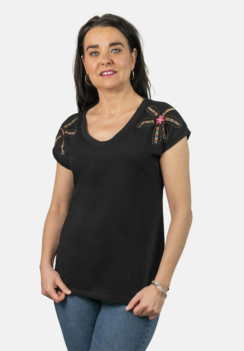 Camiseta negra de cuello en V con diseños coloridos de cuentas y bordados en los hombros, mangas cortas y un corte relajado. Llevada con jeans azules.