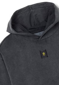 Sudadera con capucha gris de textura suave, con un bolsillo frontal y un logotipo de mano amarillo en un parche negro cerca del cuello.