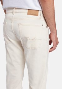 Jeans in denim bianco con taglio dritto, dotati di tasche posteriori con cuciture sottili, una patch in pelle sulla cinta e dettagli in metallo.