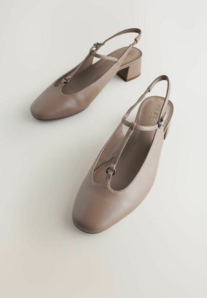 Scarpe slingback beige in pelle con punta quadrata, design a cinturino a T e tacco basso a blocco. Presentano dettagli hardware minimi per un tocco aggiuntivo.