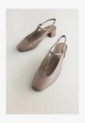 Bež kožne slingback cipele s četvrtastim vrhom, T-remenom i niskom blok petom. Imaju minimalne metalne detalje za dodatni ukras.