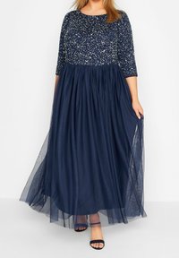 Tmavě modré večerní šaty mají zdobený korzet a splývavou tylovou sukni, s tříčtvrtečními rukávy a mírně áčkovým střihem.