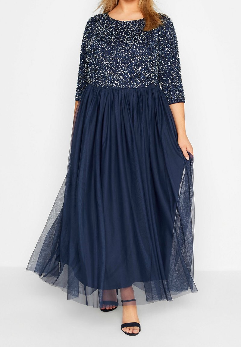 Tmavě modré večerní šaty mají zdobený korzet a splývavou tylovou sukni, s tříčtvrtečními rukávy a mírně áčkovým střihem.