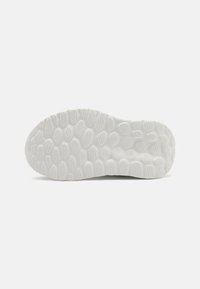 Semelle de chaussure en caoutchouc blanche présentant des motifs de traction texturés et un design ondulé, mettant en valeur une finition lisse et des bords arrondis.