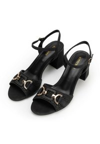 Schwarze Absatzsandalen mit einem strukturierten Stoffriemen, Einkerbungen in Gold und einem Blockabsatz. Verstellbarer Knöchelriemen inklusive.