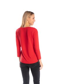 Czerwona bluzka z długimi rękawami, o szerokim dekolcie i prostym wykończeniu. Wykonana z miękkiego materiału, zestawiona z czarnymi dżinsami; gładka tekstura i prosty design.