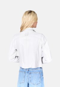 Witte leren cropped jack met een puntige kraag, een slim-fit ontwerp en zichtbare stiksels, gecombineerd met high-waisted denim jeans.