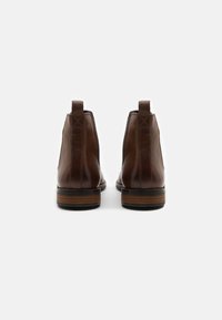 Hnědé kožené kotníkové boty s lesklým povrchem, elastickými bočními panely a vrstvým dřevěným podpatkem. Obsahují poutko pro snadné obouvání.