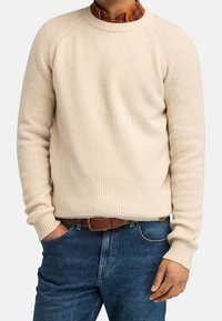 Maglione a coste color crema con scollo rotondo e maniche raglan, abbinato a una cintura marrone e jeans blu. Tessuto strutturato e silhouette aderente.