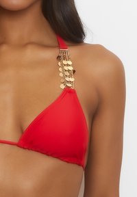 Červený bikiny top s trojúhelníkovými košíčky, zdobený zlatými řetízky s kulatými akcenty na ramínkách. Hladká, lehká tkanina.