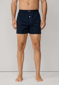 Námořnické modré kostkované plavky s elastickým pasem a knoflíkovým zapínáním, s vertikálními zelenými pruhy a lehkým materiálem.