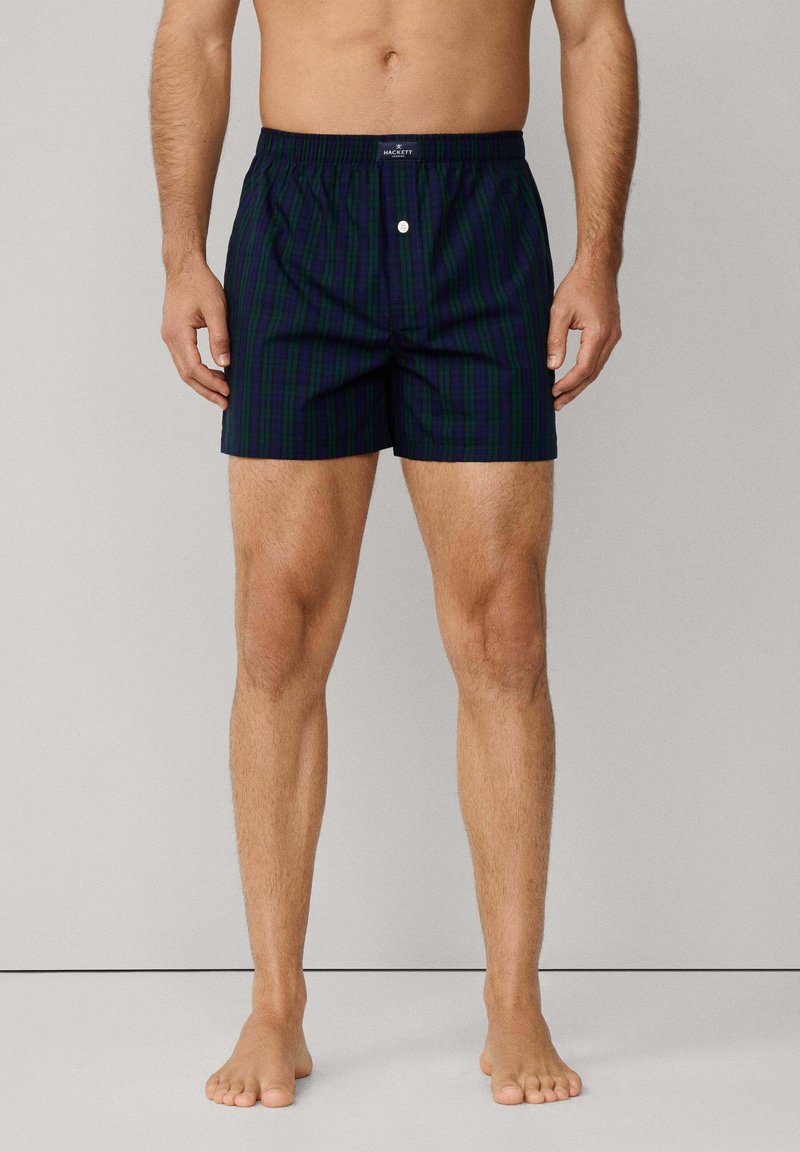 Námořnické modré kostkované plavky s elastickým pasem a knoflíkovým zapínáním, s vertikálními zelenými pruhy a lehkým materiálem.