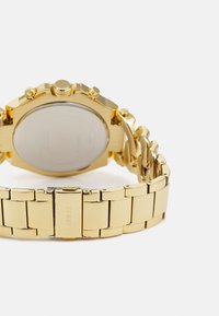 Montre-bracelet en métal doré avec un grand boîtier rond, des cadrans de chronographe et un bracelet à maillons poli avec un fermoir à boucle.