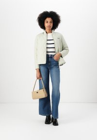 Lichtgroene gewatteerde jas, gestreepte top met lange mouwen, hooggepolstere blauwe wijdte jeans, beige handtas en zwarte enkellaarzen.