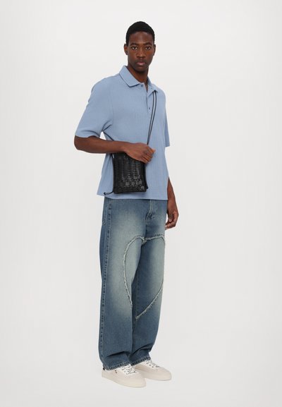 Polo azzurro chiaro a maniche corte con finitura testurizzata, abbinato a jeans denim a vestibilità comoda con un taglio a forma di cuore e sneakers bianche.
