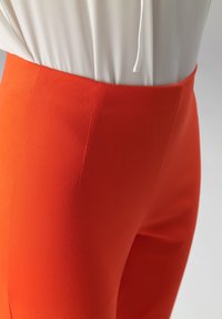 Oranje rekbare stofbroek met een gladde textuur en een aangesloten ontwerp, voorzien van een hoge tailleband en een naaddetail aan de zijkant.