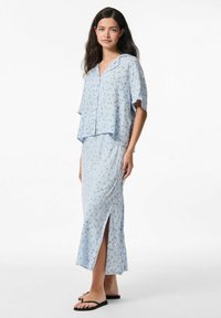 Šviesiai mėlynas gėlių dviejų dalių komplektas, susidedantis iš trumpų mygtukų viršaus su trumpomis rankovėmis ir ilgos sijono su šoniniu plyšiu bei švelnia tekstūra.