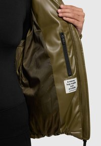 Olive green jacket with a smooth, glossy inner lining. Features a zip pocket and a label with text. Soft, padded fabric for warmth.