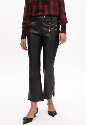 Black faux leather flared pants feature front zip pockets with gold-tone zippers, smooth texture, and a fitted waist.