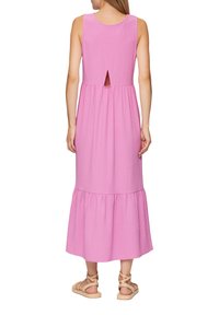 Langes pinkes Kleid aus strukturiertem Stoff, mit rundem Ausschnitt, Rückenausschnitt und gestuftem Rock. Kombiniert mit hellbraunen Riemchensandalen.