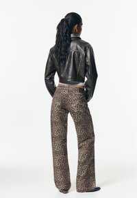 Veste courte en cuir noir avec coutures jaunes associée à un pantalon large imprimé léopard en tissu texturé avec poches latérales.