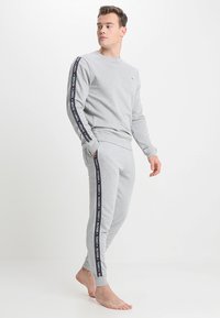 Sudadera gris y joggers a juego en una tela suave. Presenta cinta con logotipo a lo largo de las mangas y las costuras laterales; con puños y cintura de canalé.