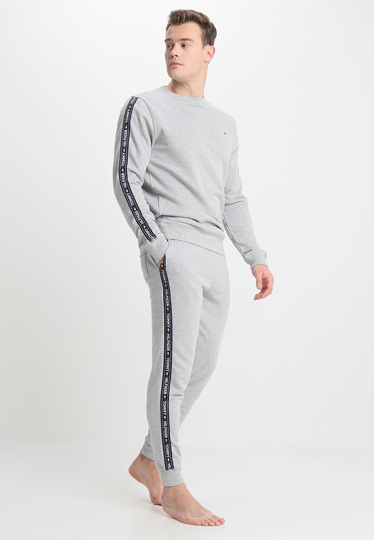 Un sweat gris et un jogging assorti en tissu doux. Présente un ruban logo le long des manches et des coutures latérales ; poignets et taille côtelés.