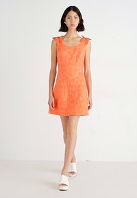 Πορτοκαλί αμάνικο φόρεμα με υφή υφάσματος, διακοσμημένο με λεπτομέρειες κορδέλας στους ώμους. Συνδυασμένο με λευκά πλατφόρμα παπούτσια. Απλή A-line σιλουέτα.