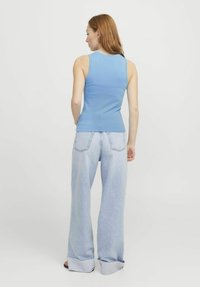 Camiseta sin mangas ajustada de color azul claro con una textura acanalada, combinada con pantalones vaqueros de corte holgado en un lavado claro que tienen los puños doblados y bolsillos traseros.