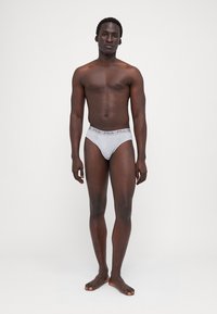 Chiloți scurți gri, cu un brad elastic texturat ce prezintă logo-ul "FILA" în gri deschis. Design simplu, material din bumbac, ajustați pe corp.