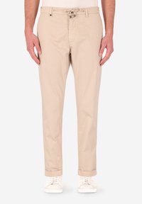 Pantaloni in cotone beige con vestibilità rilassata, dotati di vita con cordino, tasche frontali e orli arrotolati. Abbinati a sneakers bianche.