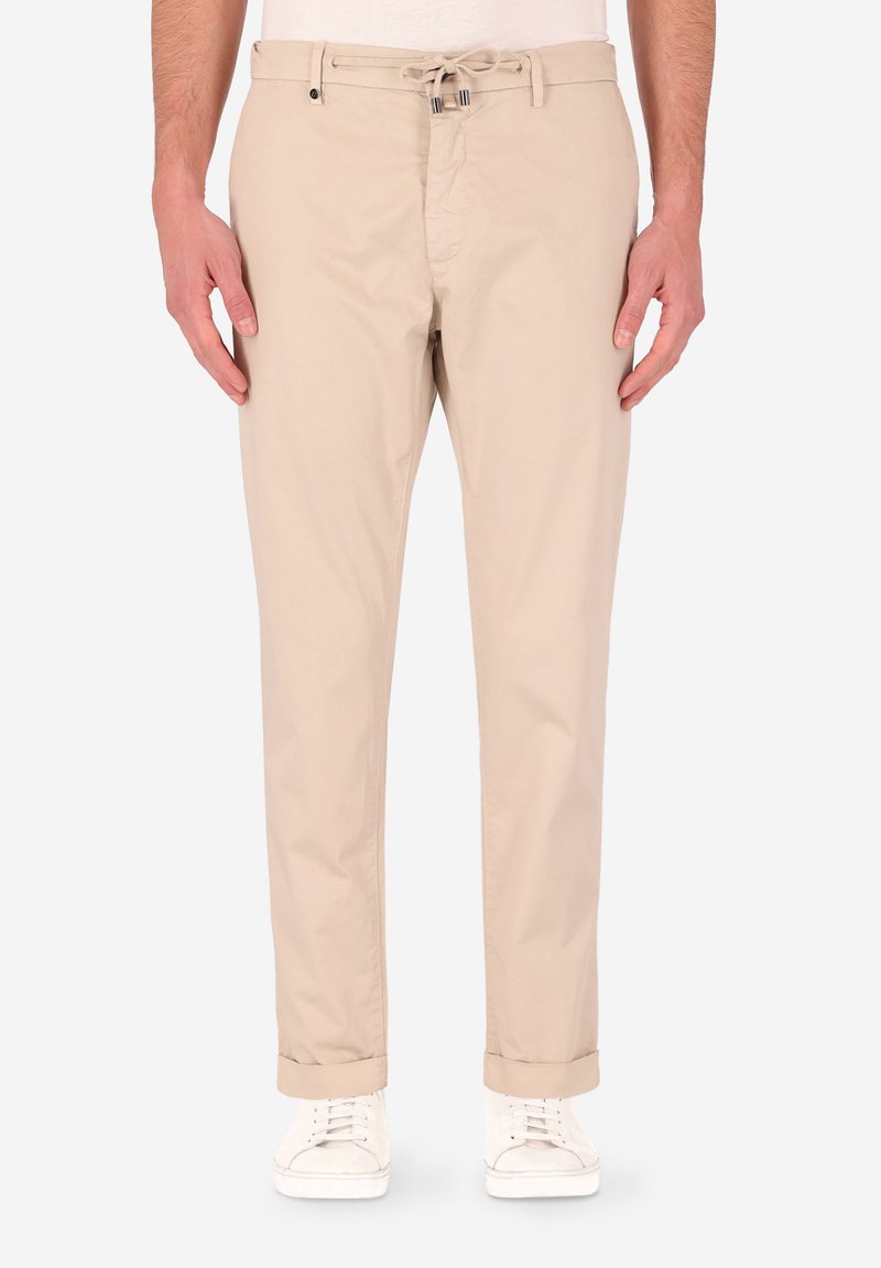 Pantaloni in cotone beige con vestibilità rilassata, dotati di vita con cordino, tasche frontali e orli arrotolati. Abbinati a sneakers bianche.