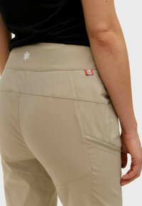 Beige outdoorbroeken met een brede, gladde tailleband met een logo. Inclusief zijzakken en ritsdetails voor functionaliteit.