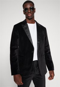 Blazer negru din catifea cu rever din satin, închidere cu un singur nasture și două buzunare. Stilizat cu un tricou alb și ochelari de soare rotunzi.