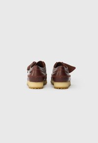 Sapatos de couro castanho com perfil baixo e sola de borracha clara. Apresentam detalhes entrelaçados e uma aba traseira para fácil calçar.