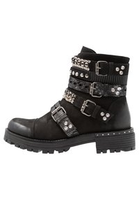 Botines negros que combinan gamuza y piel, con múltiples correas decorativas, tachuelas y hebillas. Suela de goma gruesa, diseño resistente.
