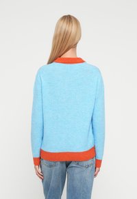 Himmelblauer Pullover mit orangefarbenem, geripptem Kragen und Saum. Verfügt über eine weiche Textur und eine entspannte Passform, mit langen Ärmeln und einem abgerundeten Ausschnitt.