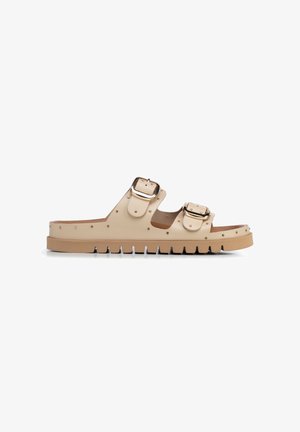 Beige slidesandaal met twee brede banden, grote goudkleurige gespen, kleine gouden studs en een dikke grof geribbelde zool voor grip.
