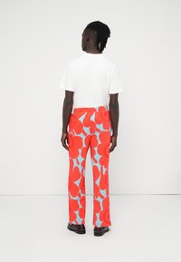 Κόκκινο και μπλε παντελόνι με χαλαρή εφαρμογή, με μεγάλα λουλουδένια σχέδια, ελαστική μέση και λεία υφή. Φορεμένο με λευκό T-shirt.