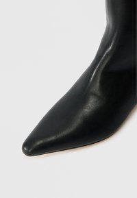 Bottine en cuir noir avec un bout pointu et une texture lisse. Design minimaliste, sans quincaillerie ou accents visibles.