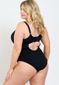 Svart baddräkt i en del med justerbara axelremmar, utklippt rygg och slät textur. Har en blygsam benöppning och en säker spänne.