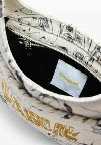 Torba od tkanine sa patentnim zatvaračem, s apstraktnim printom u crnoj i bijeloj boji, i bijelom etiketom unutra koja kaže "Desigual" u žutom tekstu.