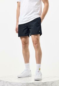 Black swim shorts made of lightweight material, featuring a smooth texture, elastic waistband, and a small logo on the leg.