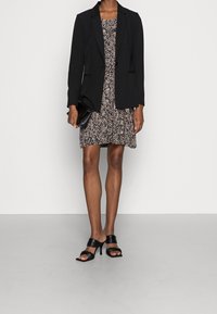 Czarny, dopasowany żakiet nałożony na sukienkę w kwiatowy wzór w odcieniach czerni, bieli i różu. Czarne sandały na obcasie z paskami. Kopertówka w dłoni.