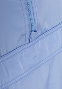 Jasnoniebieska kurtka z zamkiem błyskawicznym z przodu oraz gładką, miękką teksturą. Zawiera poziomą szwem i mały detal kieszeni.