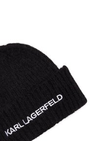 Čierna pletená čiapka vyrobená z mäkkého, štruktúrovaného materiálu so zahnutejším okrajom a vyšitým logom "KARL LAGERFELD" v bielej farbe.