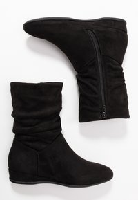 Černé semišové členkové boty s volným designem, špičatou špičkou a bočním zipem. Mají nízkou klínovou podrážku a hladkou texturu.