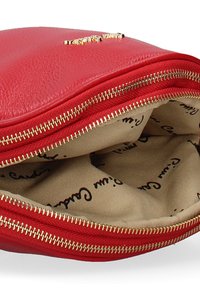 Rode leren tas met rits heeft een gestructureerde buitenkant, een goudkleurige rits en een beige interieur gevoerd met zwart bedrukt tekst.